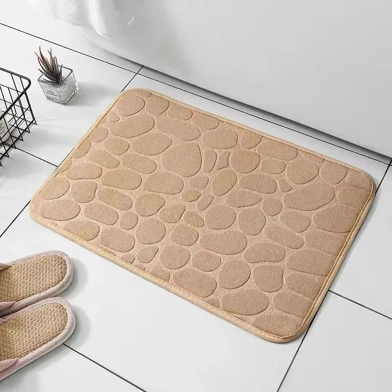 Alfombrilla de baño Variedad Online de color beige con diseño de guijarros texturizados y bordes cosidos.