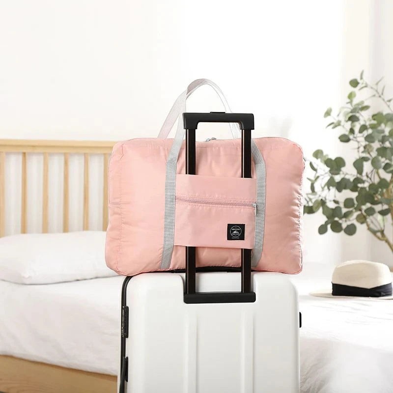 Bolsa de viaje plegable rosa de nailon resistente al agua de Variedad Online, con bolsillo frontal con cremallera y asas grises.