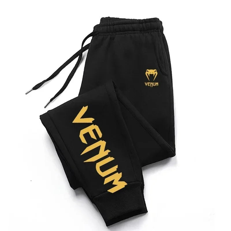 Pantalones de chándal negros Venum para hombre con logo dorado y estampado lateral. Cintura con cordón y puños acanalados.